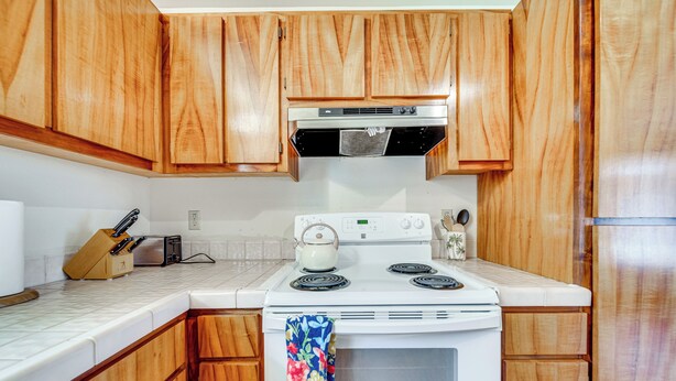 Una cocina con armarios de madera, estufa blanca y salpicadero de azulejos.