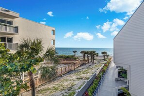 A coastal hotel with a wooden deck leading to the beach, a clear view of the ocean, and a modern building with balconies. - Beachfront Condo w/ Balcony on Manasota Key (Englewood)