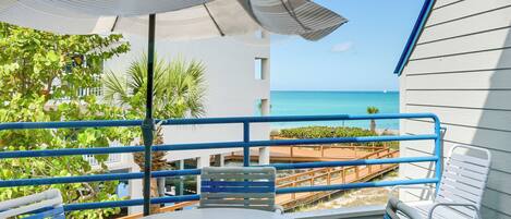Un balcon avec une table et des chaises, donnant sur une plage et l’océan.