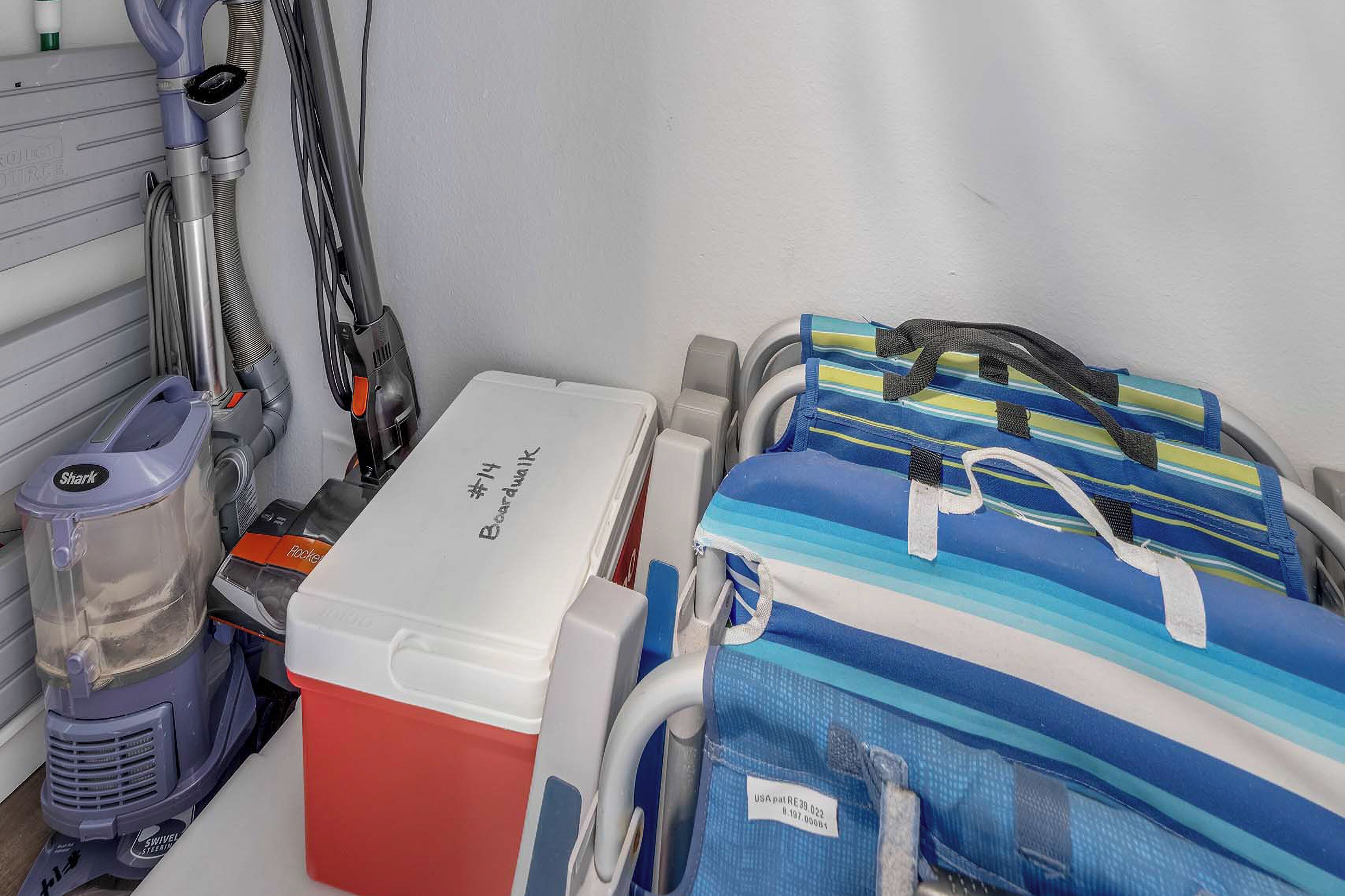 A hospital bed with a red and white storage box, a blue and white striped bag, and a vacuum cleaner against a wall.