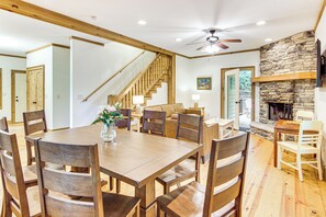 A dining area with a wooden table and chairs, a vase with flowers, a staircase, and a stone fireplace. - Your Cabin Fall Adventure Awaits in Cashiers NC (Cashiers)
