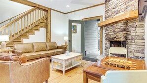 Ein gemütliches Wohnzimmer mit einer Holztreppe, einem Kamin aus Stein und einem Schachbrett.