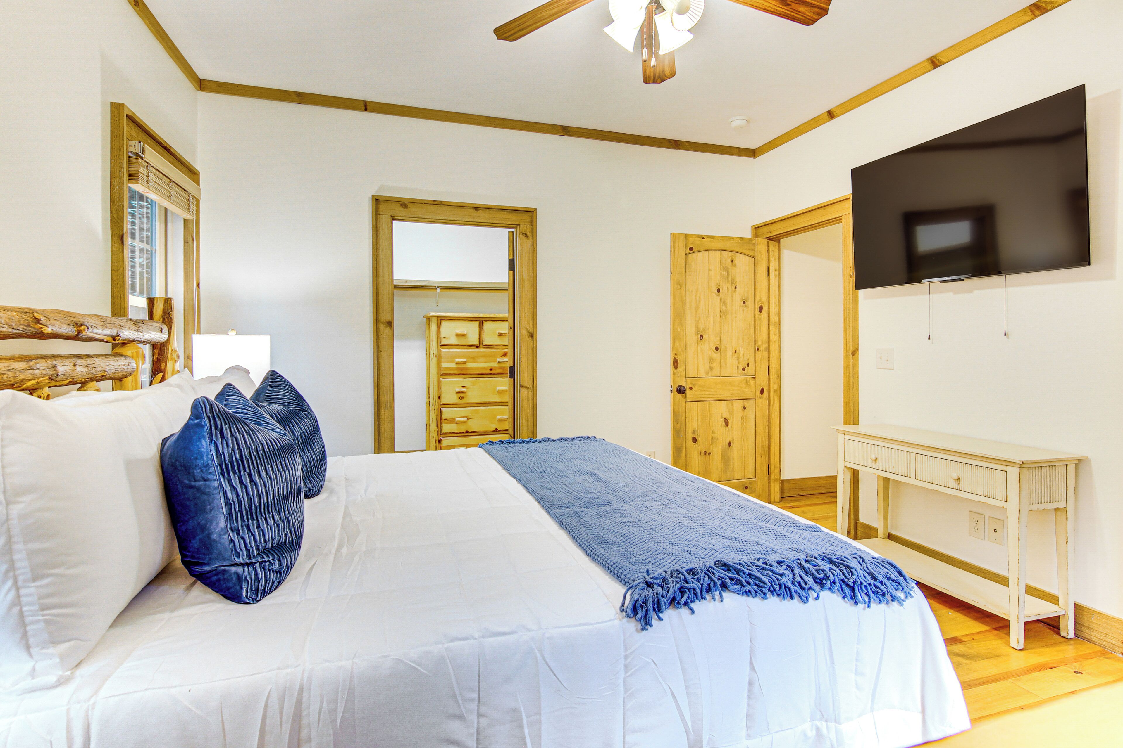 A bedroom with a bed, a TV, a wooden dresser, and a mirror.