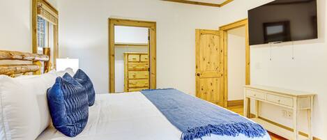 A bedroom with a bed, a TV, a wooden dresser, and a mirror.