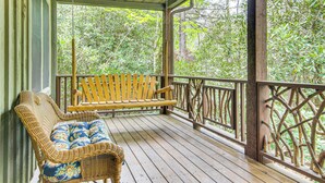 Eine Veranda mit Korbstuhl und Bank, umgeben von Holzgeländern und Blick auf dichtes Grün.