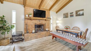 A cozy dining area with a wooden table and chairs, a fireplace, and a television mounted on the wall. - Near Fossil Creek & Trails: Scenic Pine Cabin! (Pine)