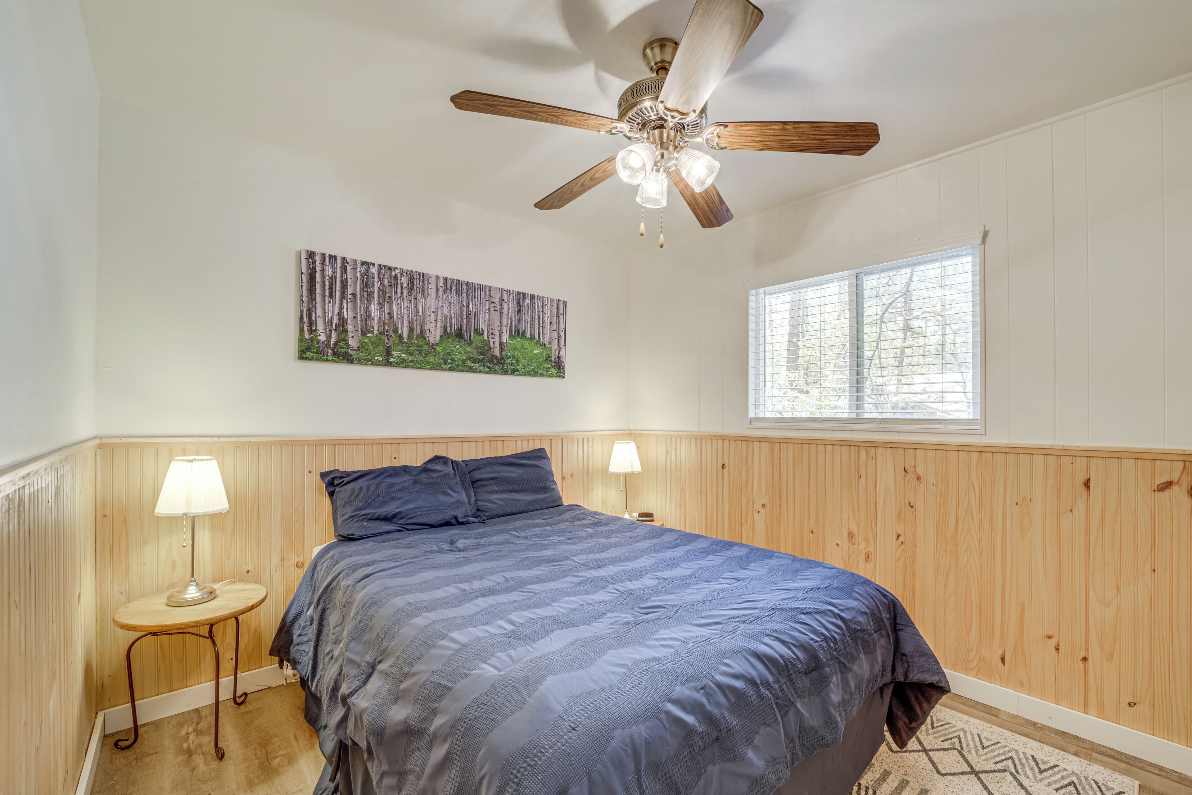 Ein Schlafzimmer mit Bett, Deckenventilator, Fenster und einem Wandbild.