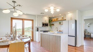 A modern kitchen with white cabinets, a central island, and a view to the outdoors. - Lake Lawtonka View: Mountaintop Medicine Park Home (Medicine Park)