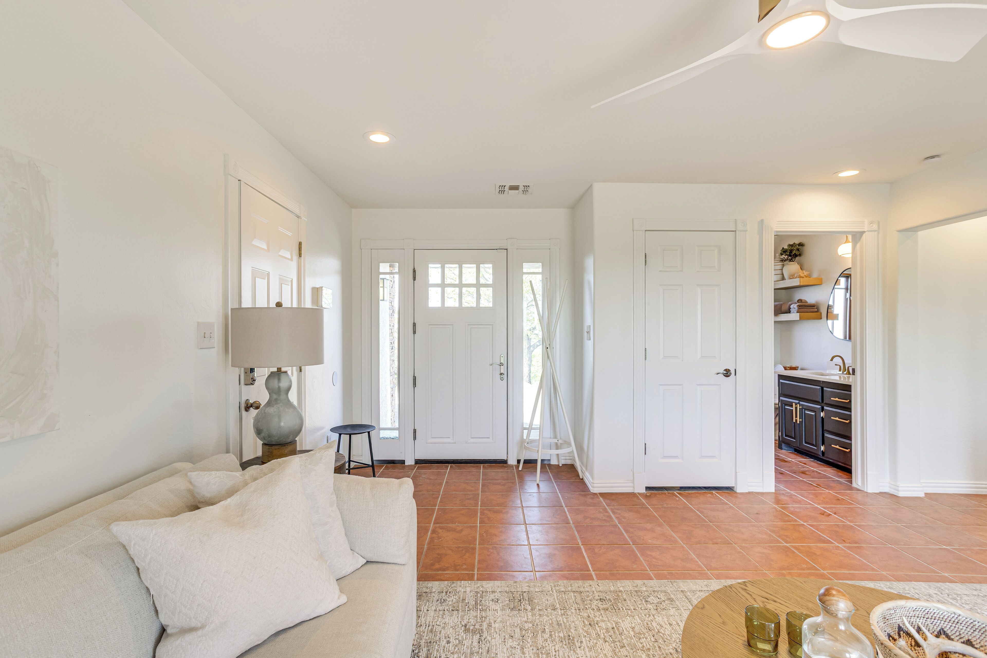 A spacious living room with a sofa, a coffee table, and a lamp. There is a door leading to a kitchen area.