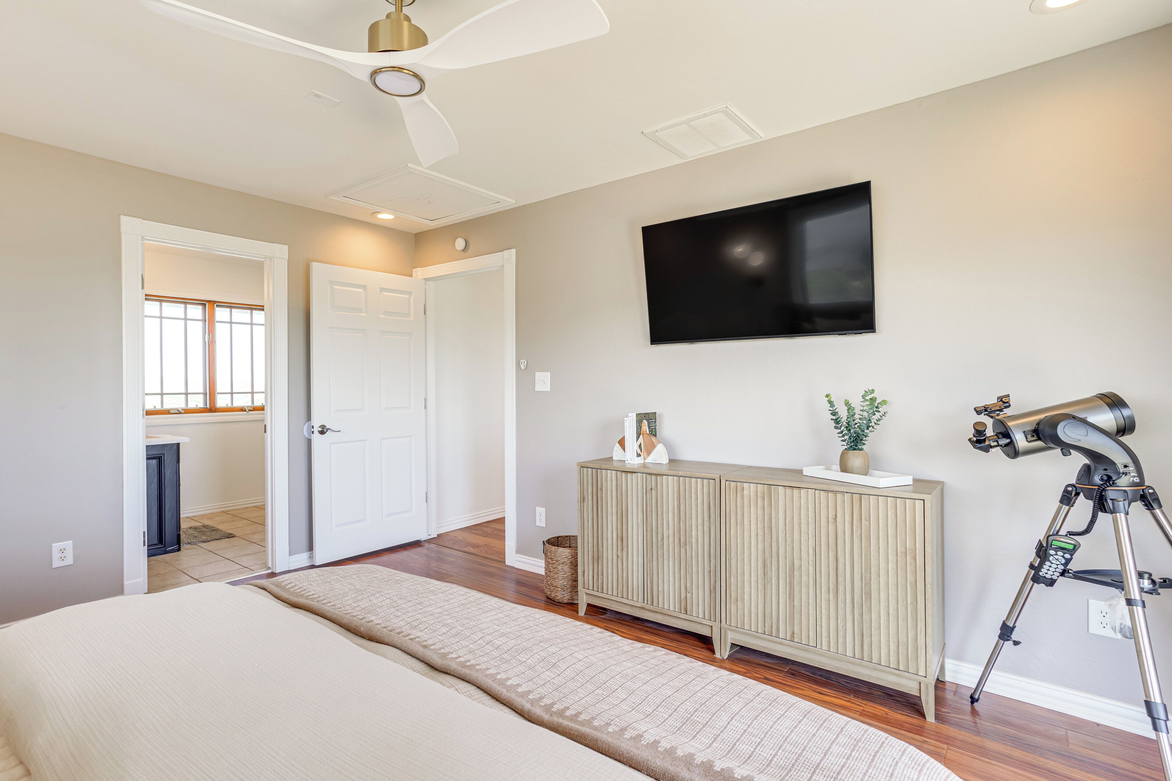 A bedroom with a bed, a ceiling fan, a TV, a cabinet, and a telescope.