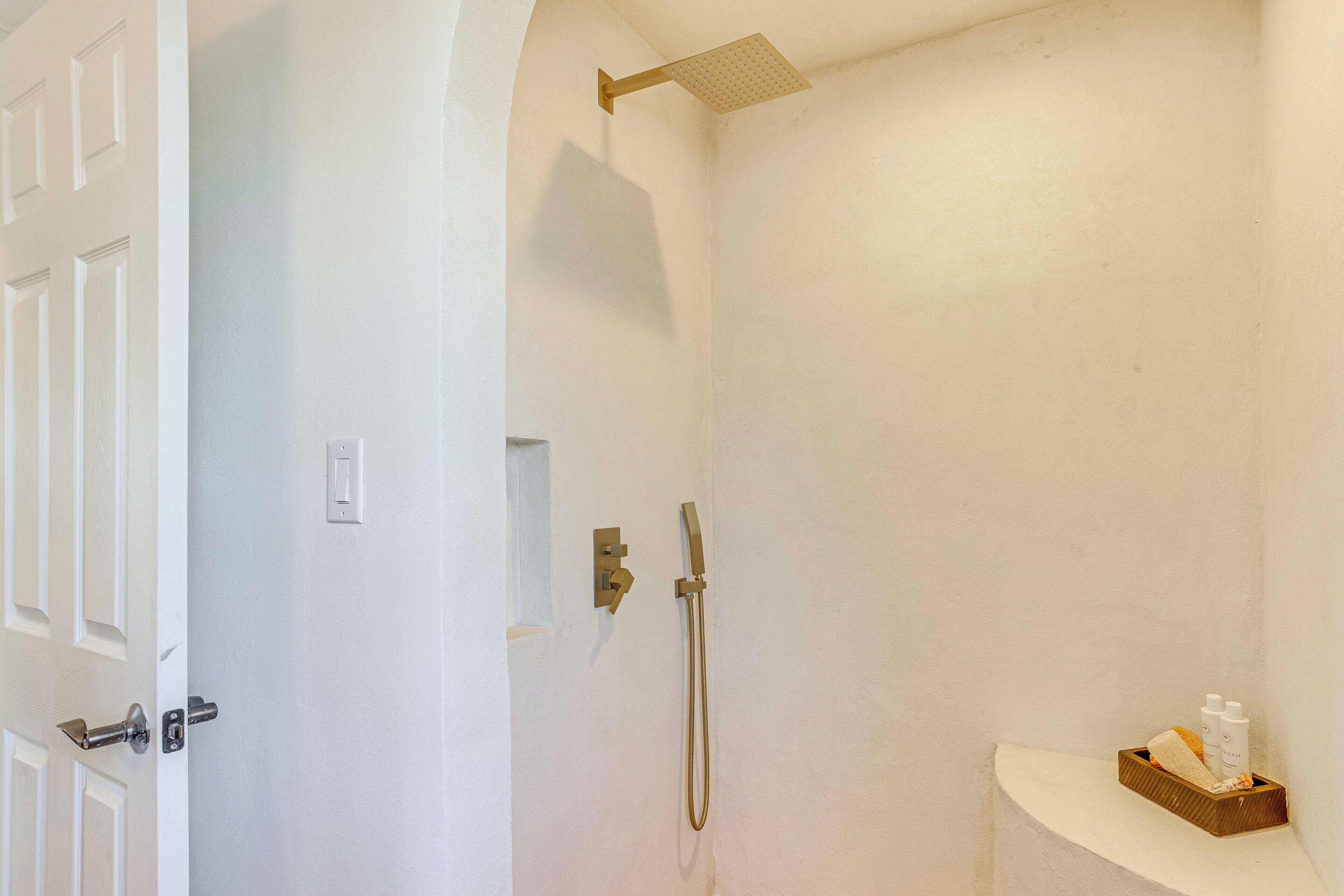 Un baño con ducha, una puerta y un estante pequeño con artículos de aseo.