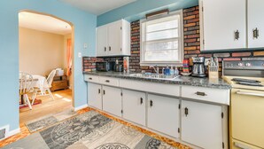 Cozinha com armários brancos, painel de backsplash de tijolos, janela com persianas e fogão.