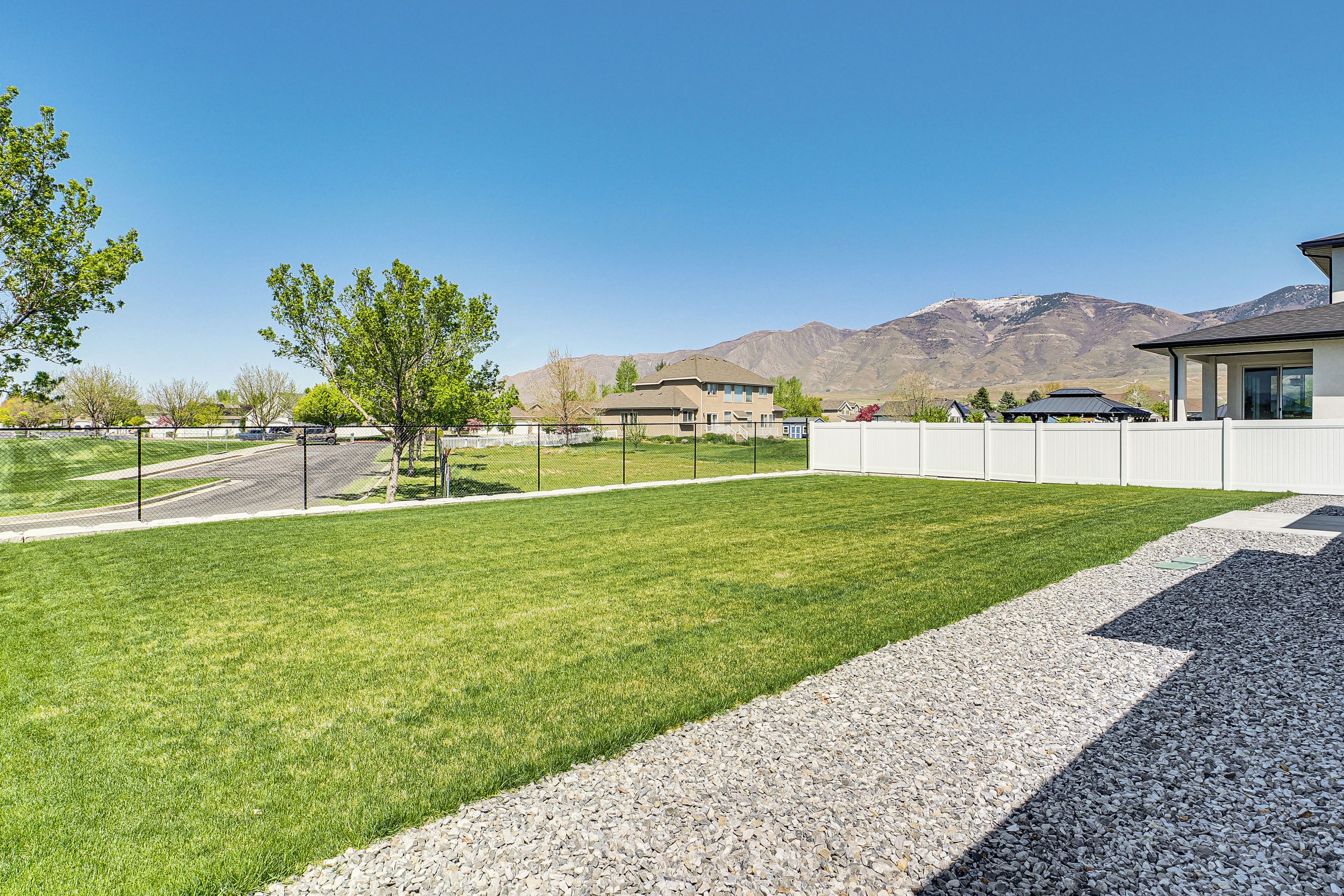 A residential area with a well-maintained lawn, a gravel pathway, and a view of mountains in the background.
