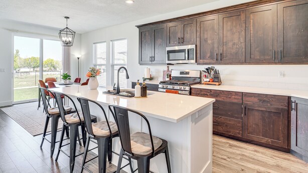 A modern kitchen with dark wooden cabinets, a large island with bar stools, a built-in microwave, and a gas stove. - 6 Mi to Great Salt Lake: Mtn-view Retreat! (Tooele)
