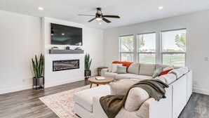 A modern living room with a sectional sofa, a flat-screen TV, a ceiling fan, and large windows. - 6 Mi to Great Salt Lake: Mtn-view Retreat! (Tooele)