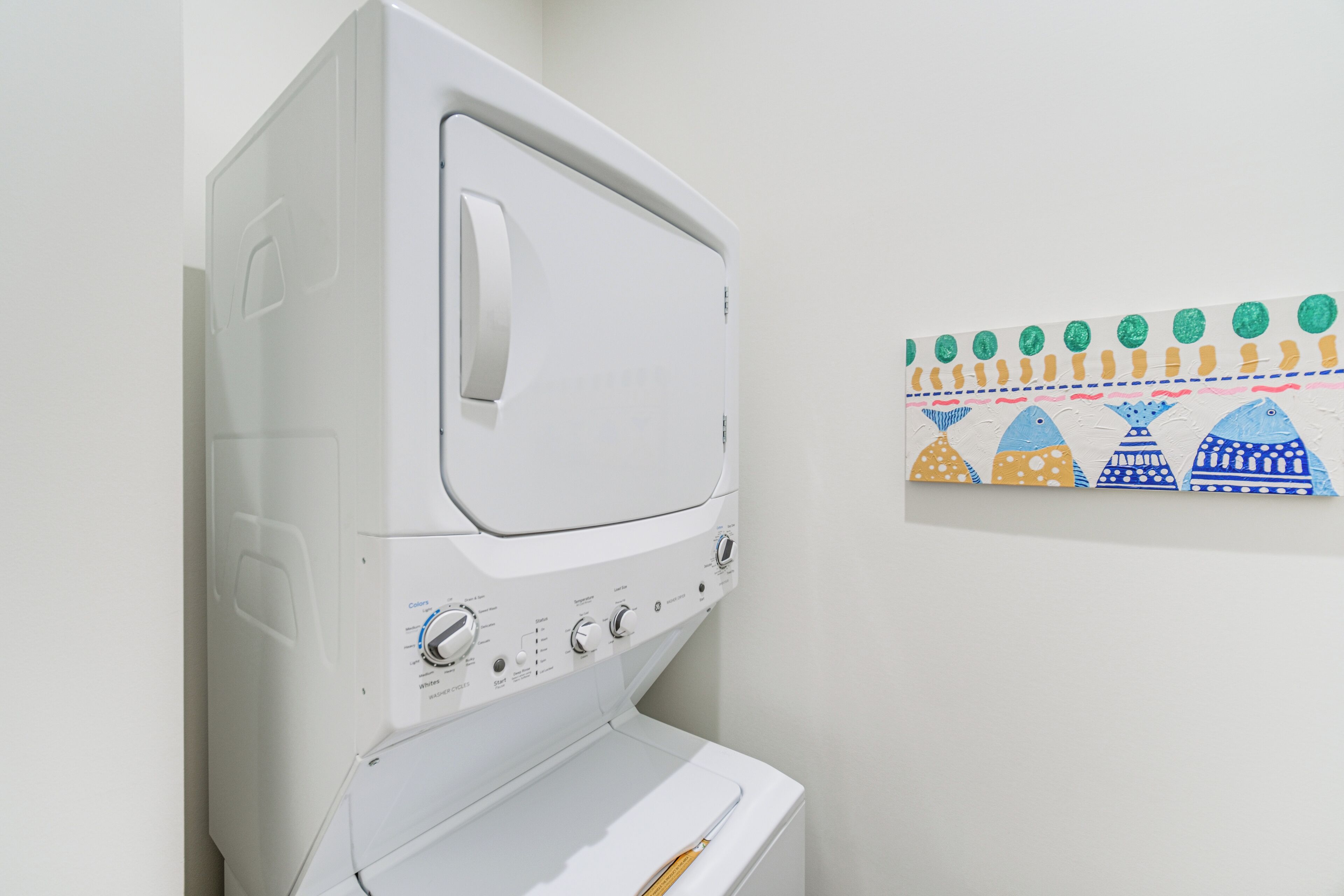 Una lavadora blanca en una habitación con un cuadro en la pared con motivos de peces.