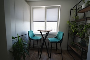 Une pièce d’angle avec une fenêtre, deux fauteuils de couleur turquoise, une petite table et une étagère pour les plantes.