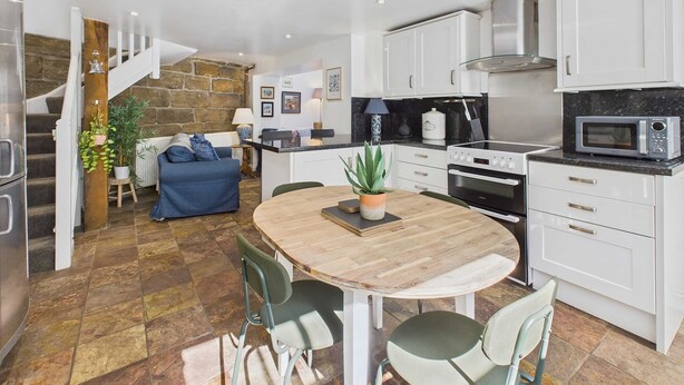 Une cuisine moderne avec des meubles blancs, un four à micro-ondes et une cuisinière. On y trouve une table à manger avec des chaises et une plante en pot.