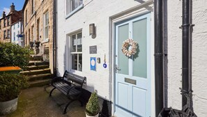 Un bâtiment blanc avec une porte bleue, un banc et une petite plante en pot.