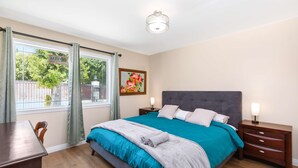 A bedroom with a bed, a nightstand, a desk, and a window with curtains. - Sunny Spanish Villa Pool Parking Privacy (Hacienda Heights)