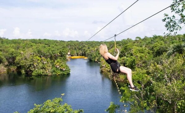 A person zip-lining over a river surrounded by dense greenery. - Luxury Penthouse w Private Pool Stunning Views (Tulum)