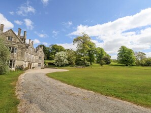 A stone building with a gravel driveway leading to a grassy area with trees. - Fallow (Dorchester)