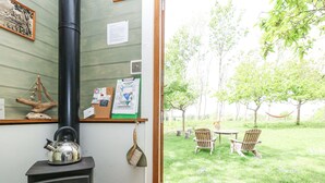 Una stanza con una stufa a legna, vista su un giardino erboso con sedie e un'amaca, e un avviso con vari documenti e una scopa appesa.