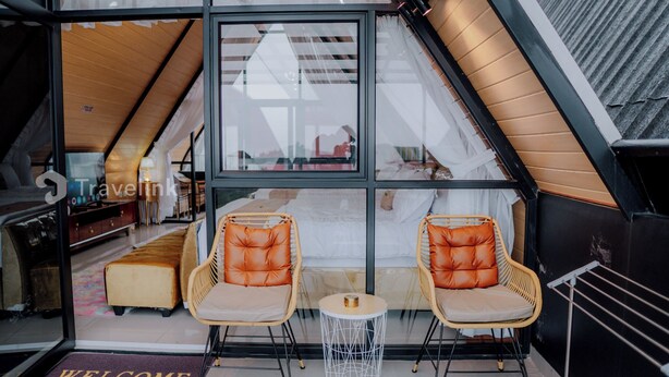Een gezellige kamer met een glazen wand, twee rieten stoelen, een klein rond tafeltje en een vloermat.