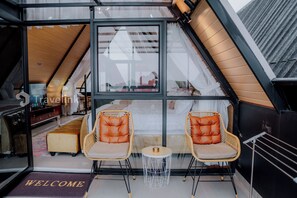 A cozy room with a glass wall, two wicker chairs, a small round table, and a welcome mat. - D'Sultan Villa Dieng By Travelink (Dieng Kulon)