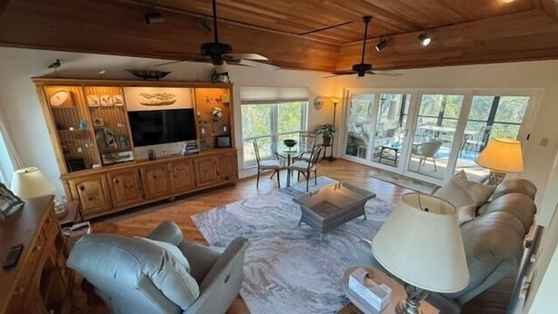 A spacious living room with a wooden ceiling, a television, a dining area with chairs, and large windows. - Black Skimmer Home | Relaxing Sanibel Escape, Walk to Beach (Sanibel)
