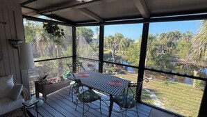 A covered patio with a table and chairs, a lamp, and a view of a natural landscape. - Black Skimmer Home | Relaxing Sanibel Escape, Walk to Beach (Sanibel)