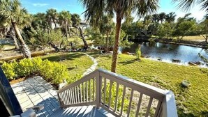 A deck with a view of a pond, surrounded by greenery and palm trees. - Black Skimmer Home | Relaxing Sanibel Escape, Walk to Beach (Sanibel)