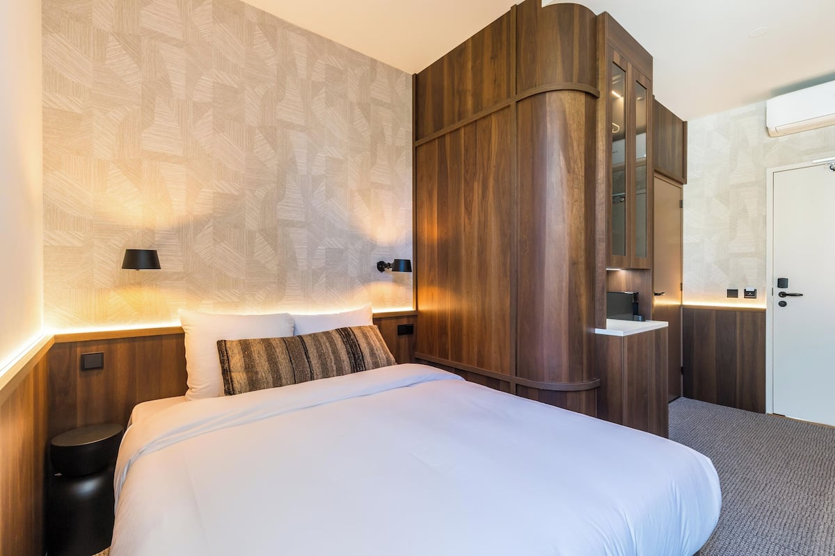 A hotel room with a large bed, wooden wardrobe, and a small bedside table.