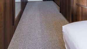 A hotel hallway with a carpeted floor, wooden walls, a large mirror, and a small kitchenette area with a sink and countertop.