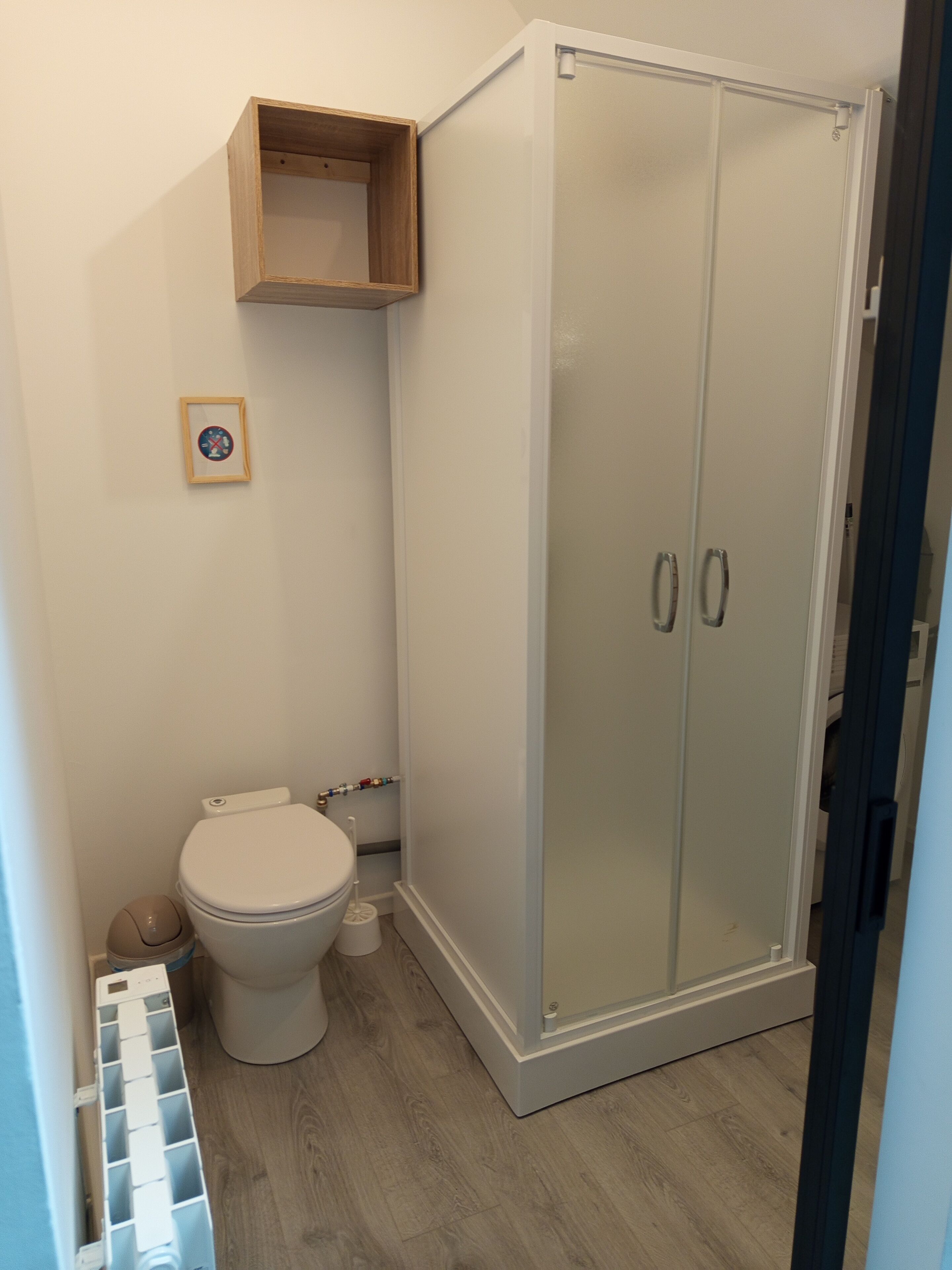 Un baño con inodoro, cabina de ducha y un pequeño estante de madera sobre el inodoro.