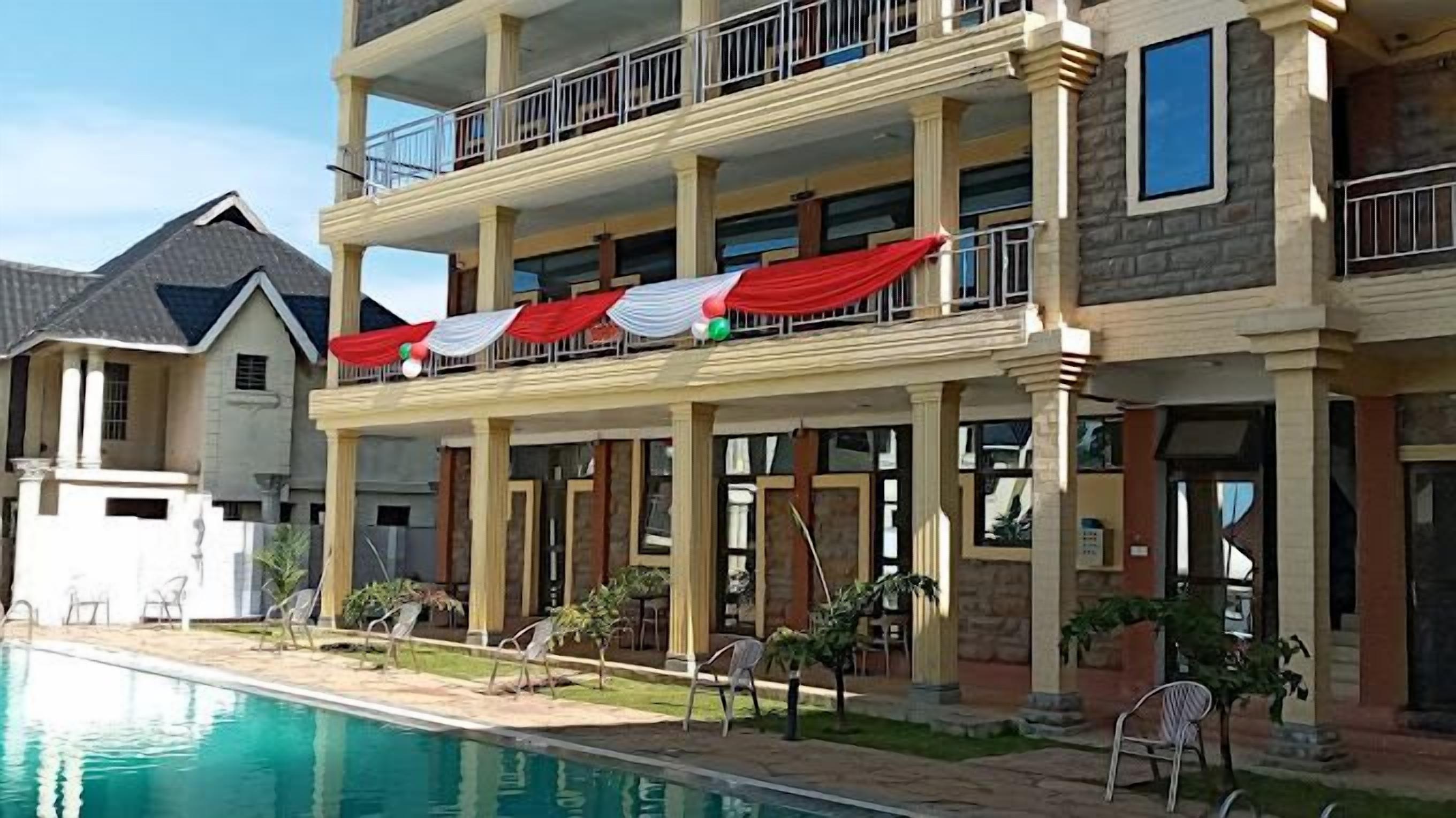 Un immeuble résidentiel à plusieurs étages doté d’une piscine, d’un espace extérieur aménagé et d’un balcon agrémenté de rideaux rouges et blancs.