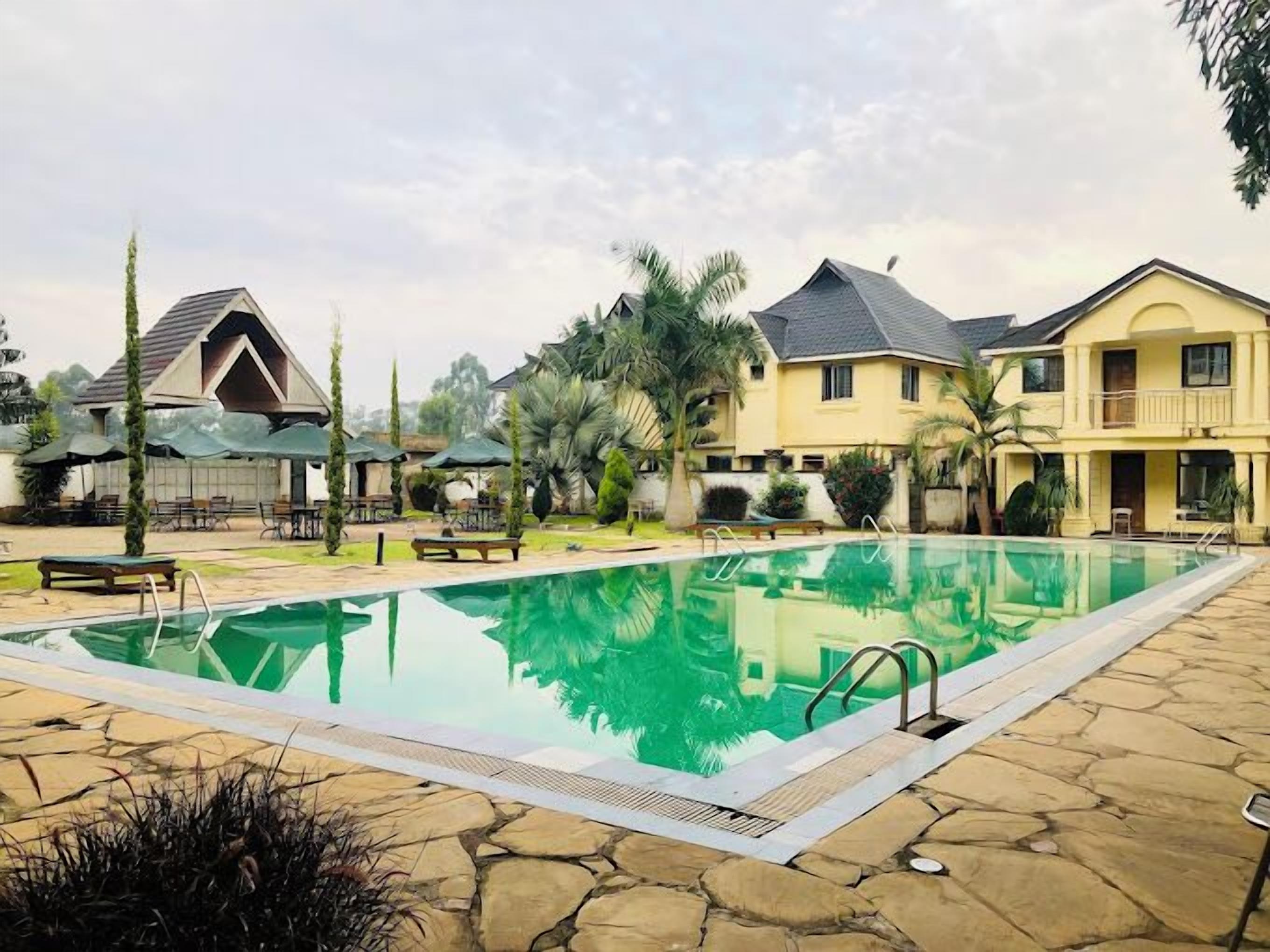Una piscina rectangular con agua cristalina, rodeada de baldosas de piedra y palmeras.