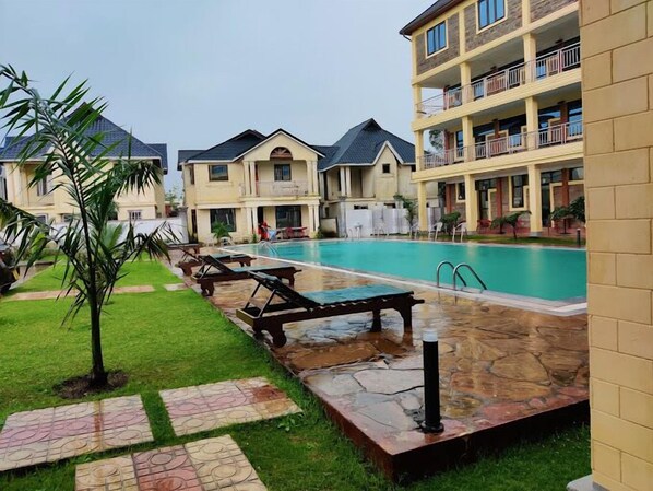 A hotel with a swimming pool, outdoor seating, and a well-maintained lawn.