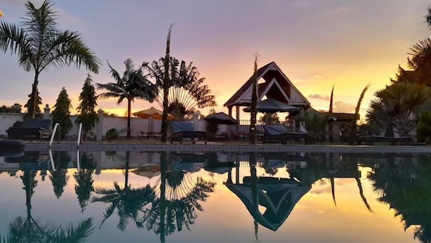 A pool reflecting palm trees and a gazebo at sunset. - Hotel Discretion LTD (Migori)