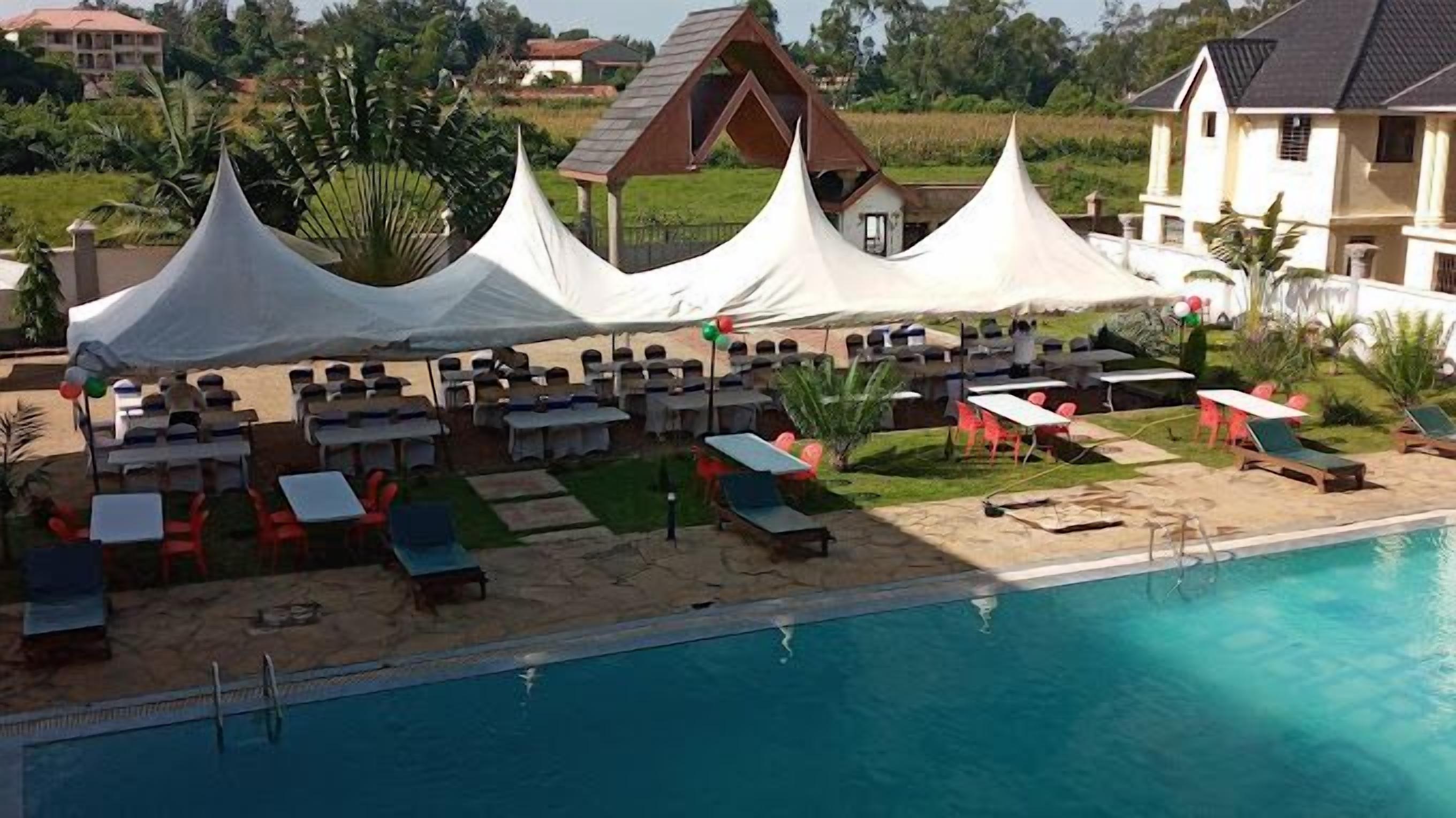 A poolside area with multiple tables and chairs, a swimming pool, and white tents.