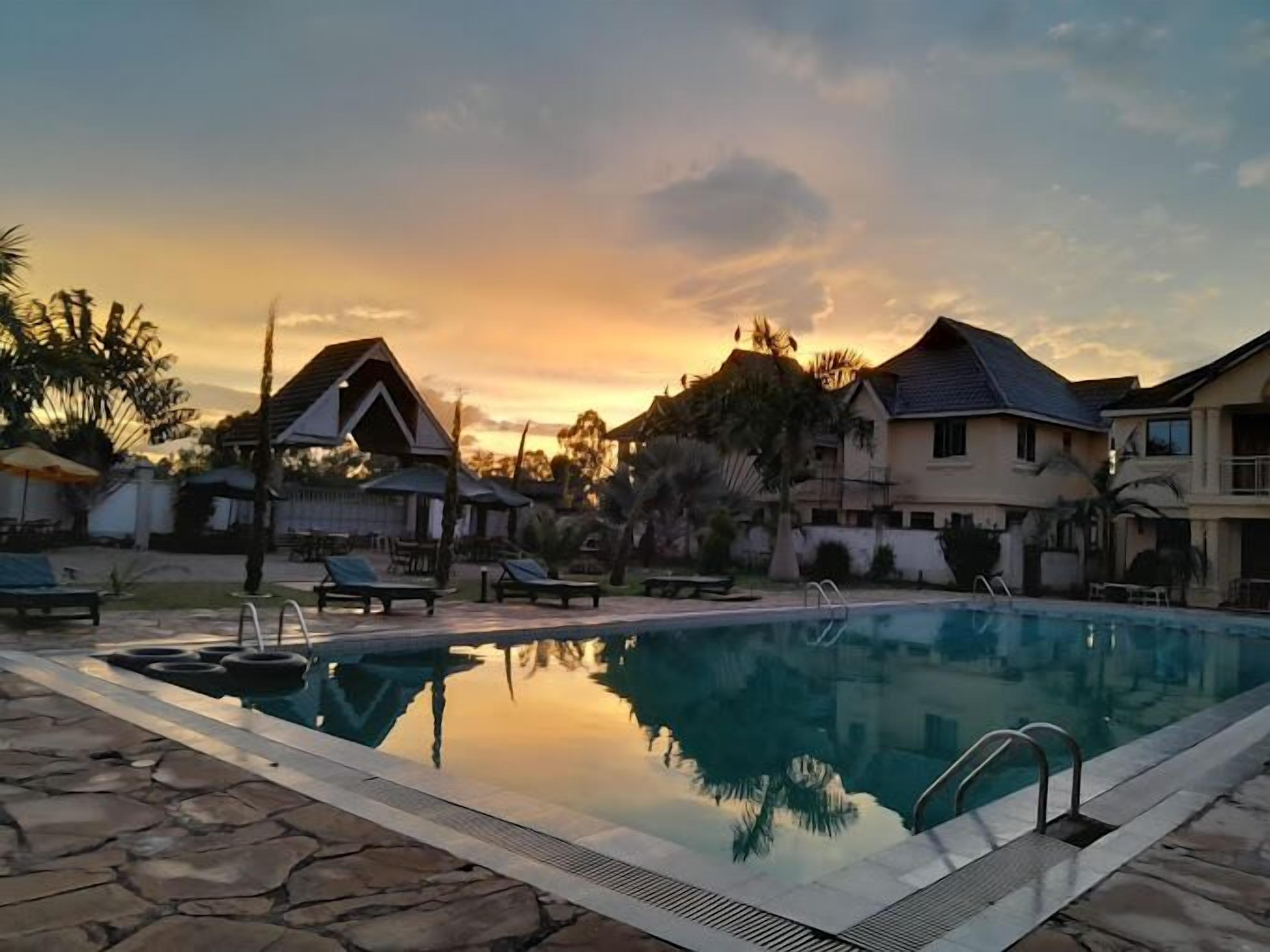 A swimming pool with lounge chairs and a stone deck, surrounded by houses and palm trees.