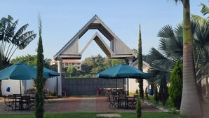 A building with a distinctive triangular entrance, surrounded by palm trees and outdoor seating with umbrellas. - Hotel Discretion LTD (Migori)