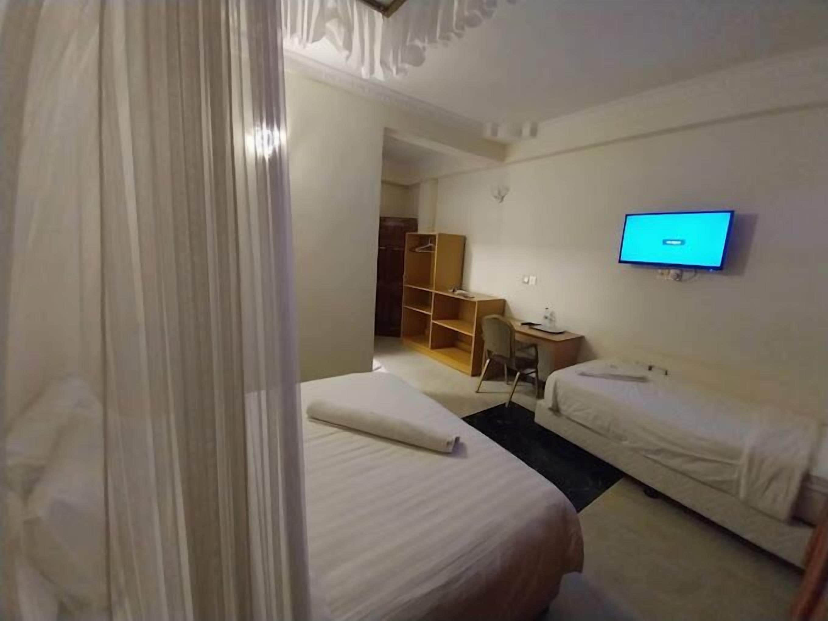 Une chambre d’hôtel avec deux lits, un bureau, une télévision et une armoire.