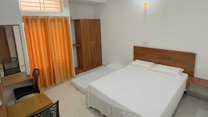 A hotel room with a bed, a desk, a chair, a wardrobe, and a ceiling fan.