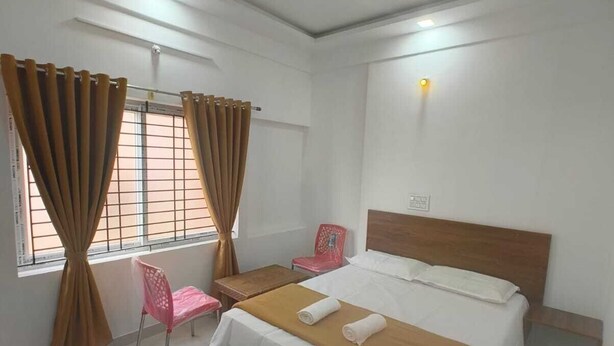 A bedroom with a bed, a chair, a table, and a window with curtains.