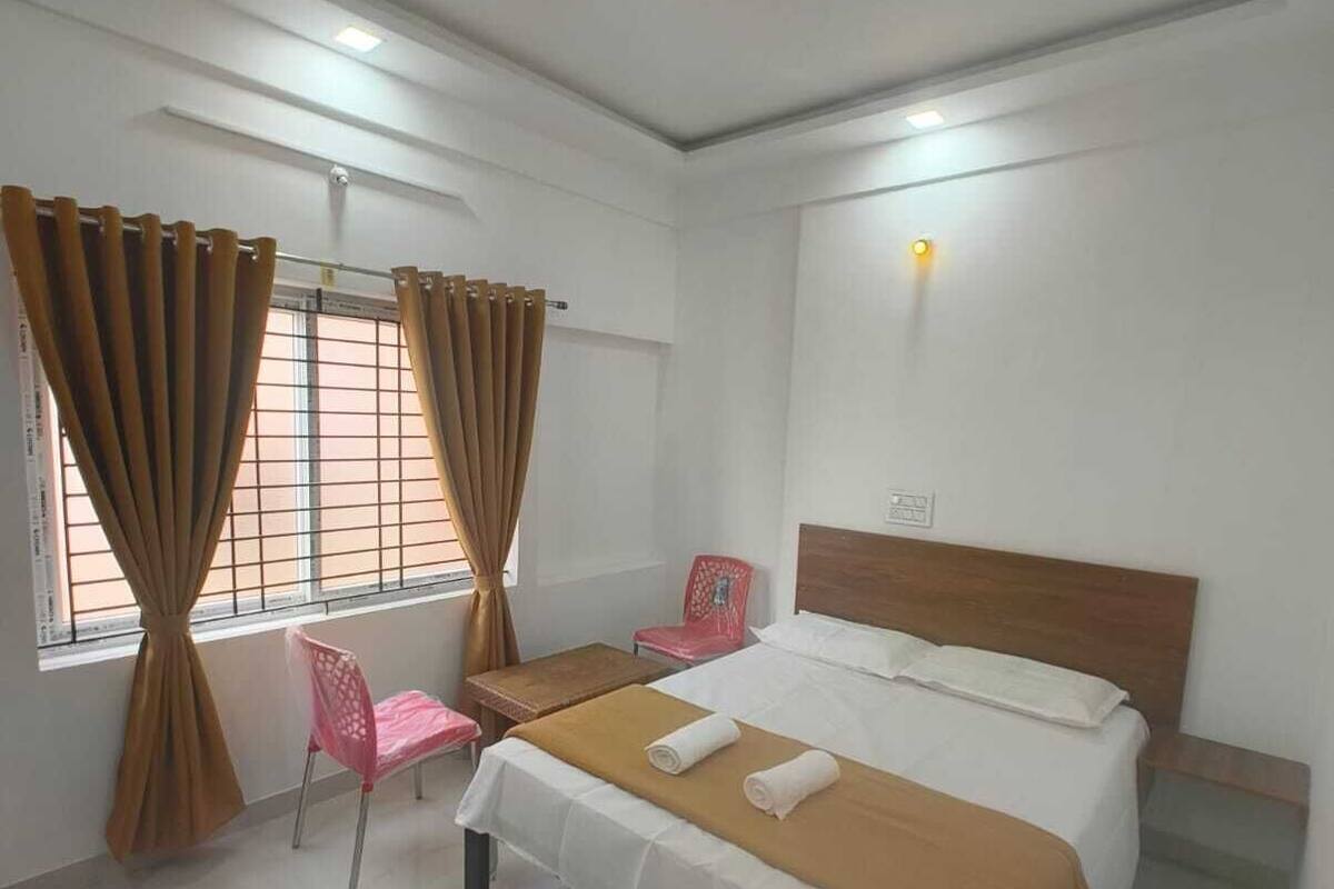 A bedroom with a bed, a chair, a table, and a window with curtains.