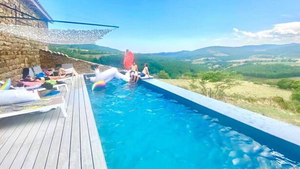 A swimming pool with a wooden deck, surrounded by a stone wall and a view of distant hills.