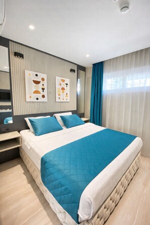 A modern hotel room with a large bed, a bedside table, a mirror, and abstract wall art. - Sky Luxe Hotel Konyaaltı (Konyaalti)
