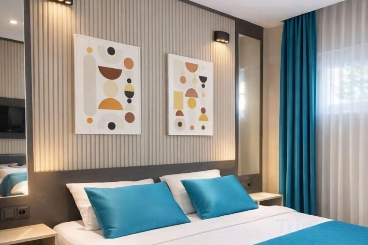 A modern hotel room with a large bed, two bedside tables, and abstract wall art.