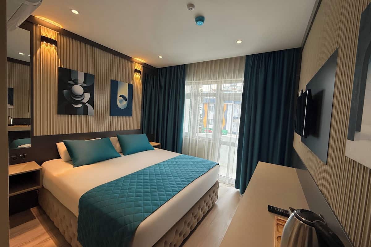 A modern hotel room with a large bed, a desk, a TV, and a view of the outside.